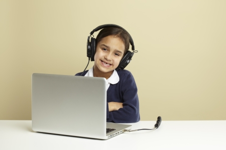 Young girl using laptop on white desk listening to musicの写真素材