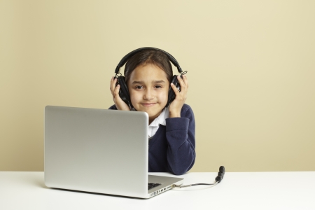 Young girl using laptop on white desk listening to musicの写真素材