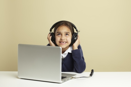 Young girl using laptop on white desk listening to musicの写真素材