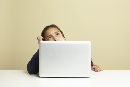 Young girl using laptop on white desk whilst thinkingの写真素材