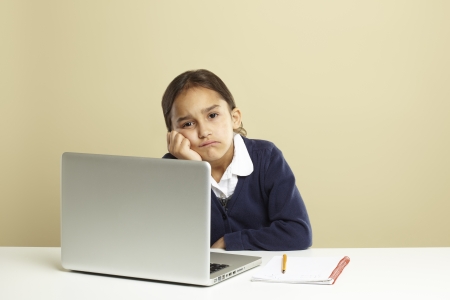 Young girl using laptop on white desk with homework looking boredの写真素材