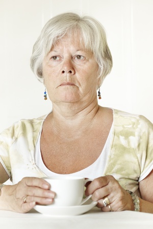 Thoughtful Senior lady sitting at table holding a cup of teaの写真素材