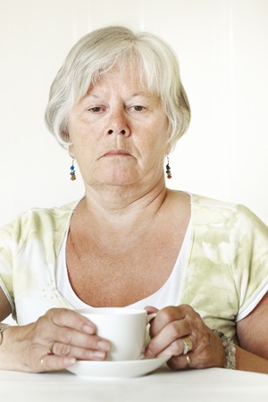 Thoughtful Senior lady sitting at table holding a cup of teaの写真素材