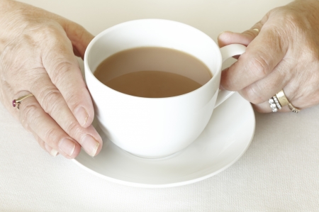 Senior womans hands holding a cup of tea on white table clothの写真素材