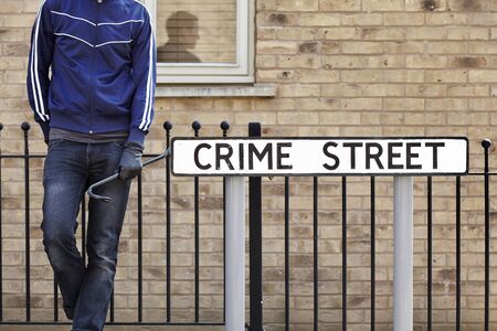 Burglar standing on street with crowbar and leather gloves next to crime street road signの写真素材