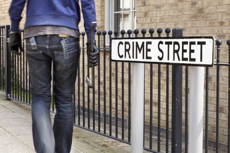 Burglar standing on street with crowbar and leather gloves next to crime street road signの写真素材