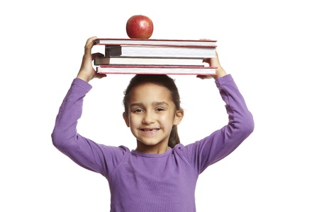 8 year old school girl with school books and apple on her head smiling on white backgroundの写真素材