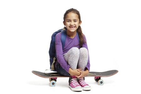 8 year old school girl with backpack sitting on a skateboard on white backgroundの写真素材