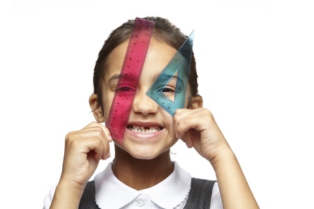 School girl with pink ruler and blue set square over her eyes smiling on white backgroundの写真素材