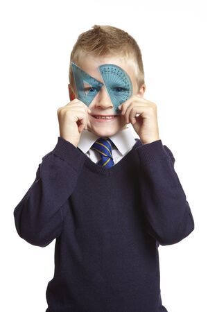 8 year old school boy with blue set square and protractor over his eyes on white backgroundの写真素材