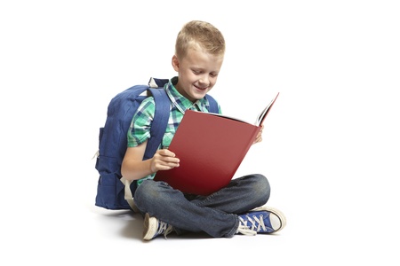 8 year old school boy sitting reading with backpack on white backgroundの写真素材