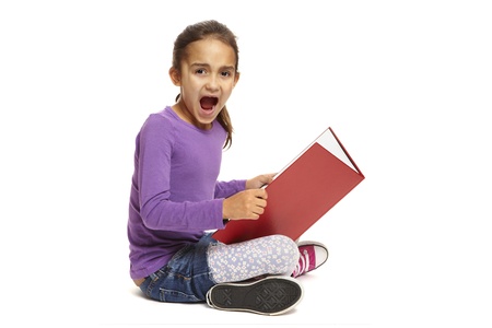 8 year old school girl sitting reading book looking shocked on white backgroundの写真素材