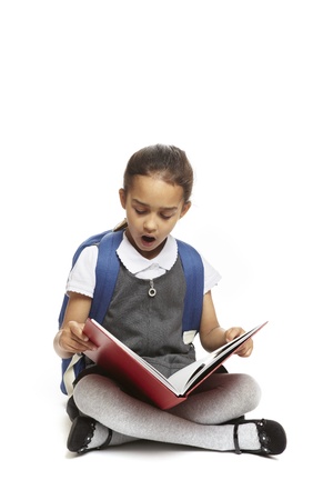 8 year old school girl sitting reading book with backpack looking shocked on white backgroundの写真素材