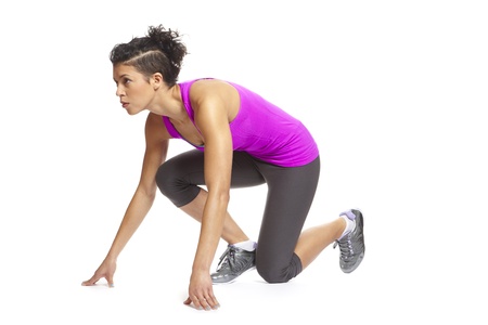Muscular young woman in starting position and ready to race in sports outfit on white backgroundの写真素材