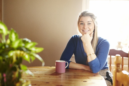 Young woman sitting at table with hot drink smiling の写真素材