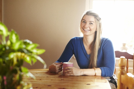 Young woman sitting at table with hot drink smiling の写真素材