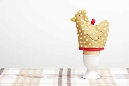 boiled egg in cup with hen egg warmer on brown table clothの写真素材