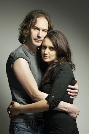 Young mixed race couple looking sad and thoughtful cuddling on plain backgroundの写真素材