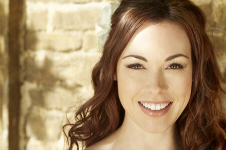 Female bride standing against sunny wall smilingの写真素材