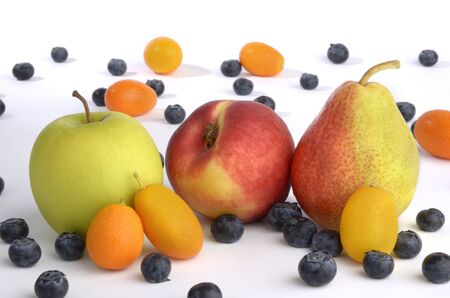 Apple, pear and orange with kumquats and blueberries against white backgroundの写真素材