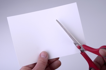 hand holding blank sheet of paper and cutting it with pair of scissors, backgroundの写真素材