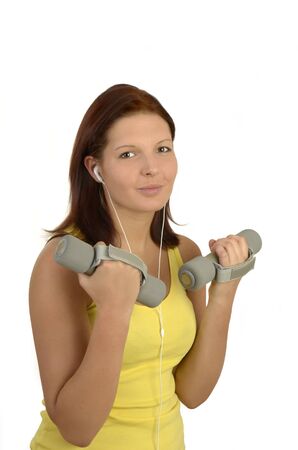 Young woman in a yellow tank top against white background during power training listen to music, isolated, portrait formatの写真素材
