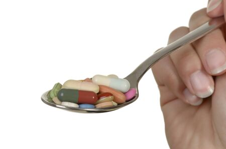 hand holding spoon wih different colorful pills, isolated, white background, copy spaceの写真素材