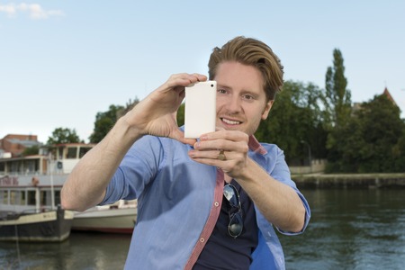 Happy young man taking pictures with smart phone, Outdoor Shotの写真素材