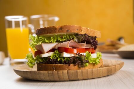 Sandwich on a white plate with turkey breast, tomato, lettuce and cheese on the tableの写真素材
