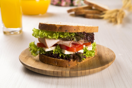 Sandwich on a white plate with turkey breast, tomato, lettuce and cheese on the tableの写真素材