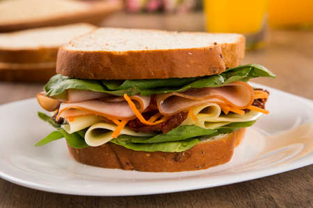 Sandwich on a white plate with turkey breast, tomato, lettuce and cheese on the tableの写真素材
