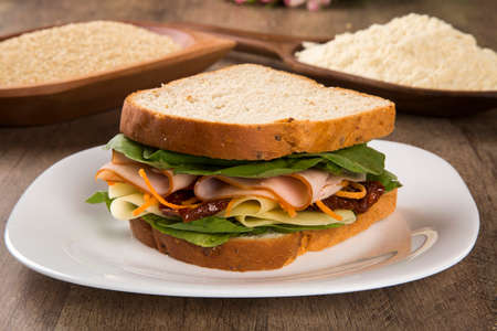Sandwich on a white plate with turkey breast, tomato, lettuce and cheese on the tableの写真素材