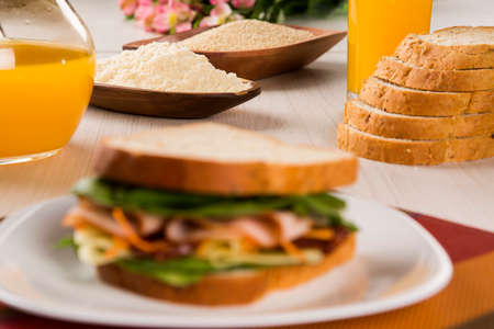 Sandwich on a white plate with turkey breast, tomato, lettuce and cheese on the tableの写真素材