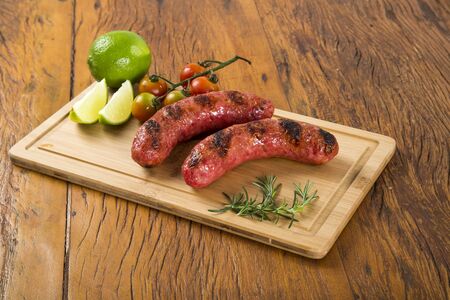 grilled sausages on the grill on the board with lemon, potatoes and tomatoesの写真素材