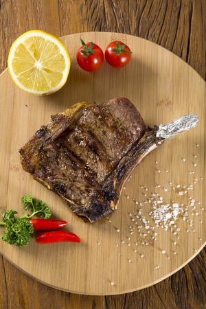 Grilled meat ribs on white plate with tomatoes chives and dark hot sauce on boardの写真素材