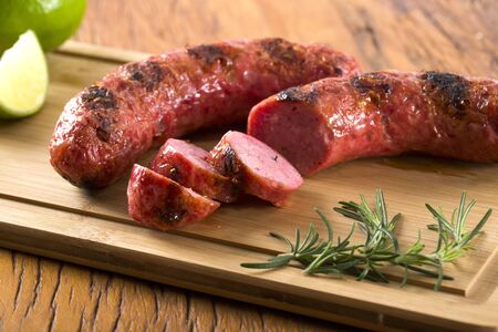 grilled sausages on the grill on the board with lemon, potatoes and tomatoesの写真素材