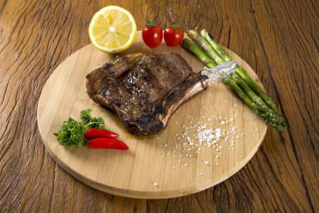 Grilled meat ribs on white plate with tomatoes chives and dark hot sauce on boardの写真素材