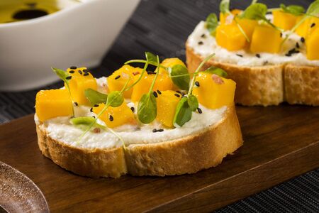Bruschetta with chopped mango, cress, basil and goat cheese on fresh baguette on the table.の写真素材
