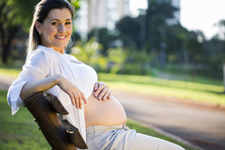 Pregnant sitting on bench in the park at sunsetの写真素材
