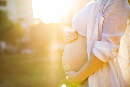 Beautiful pregnant woman in a sunset outside in the park.
