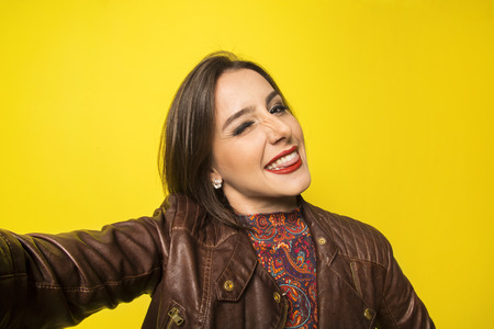 Portrait of a Beautiful successful smiling girl doing selfie  on a yellow backgroundの写真素材