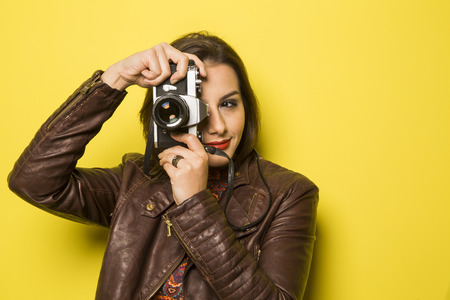 Fashion young girl makes the photo with old camera. Yellow backgroundの写真素材
