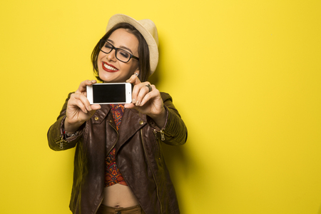 Portrait of a Beautiful successful smiling girl doing selfie  on a yellow backgroundの写真素材
