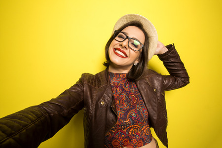 Portrait of a Beautiful successful smiling girl doing selfie  on a yellow backgroundの写真素材