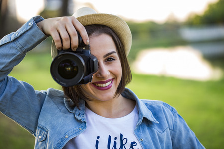 Young woman making photos with professional camera at summer green park.