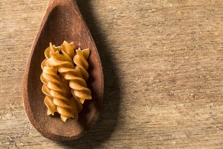 Wholemeal Fusilli into a spoon. Integral Pasta over a wooden tableの写真素材