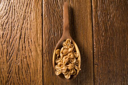 Raw farfalle or bow-tie pasta on wooden spoon. Integral Pasta over a wooden table