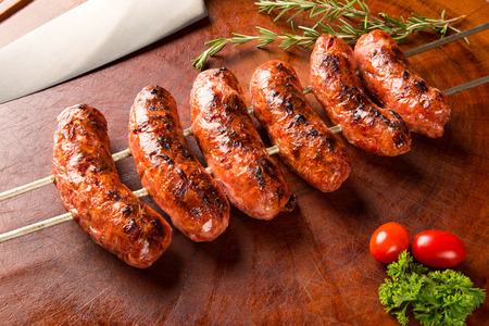 Sausages on the barbecue spit on wooden backgroundの写真素材