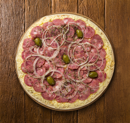 Raw pizza with pepperoni on wooden backgroundの写真素材