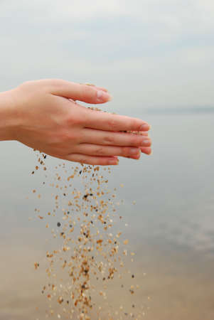 falling sand in female hands over seaの写真素材